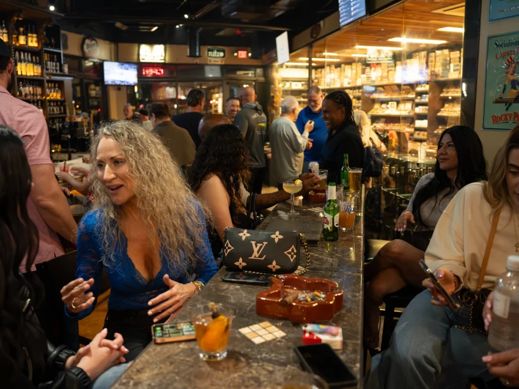 Guests chatting and drinking along the marble bar at Fox Cigar Bar Gilbert, with the humidor glowing behind