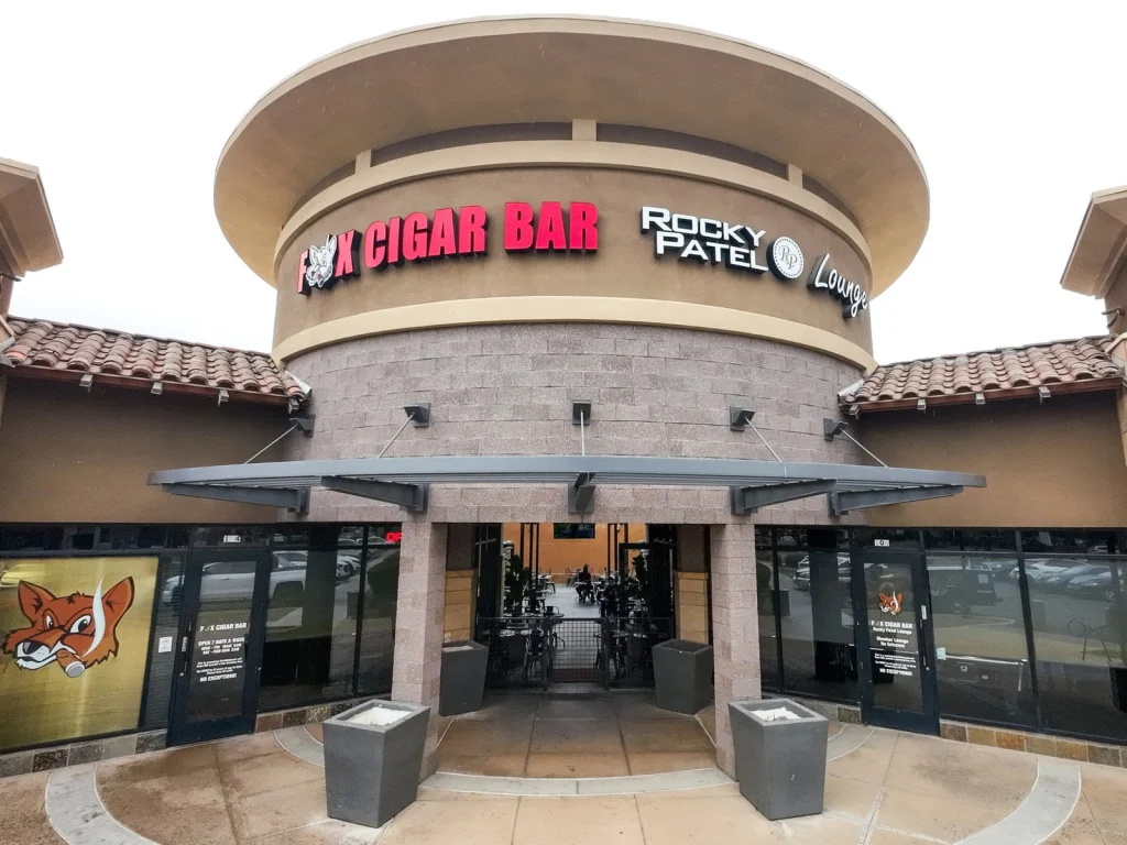 Round tan building entrance of Fox Cigar Bar Gilbert with red lettering, Rocky Patel Lounge sign and fox logo