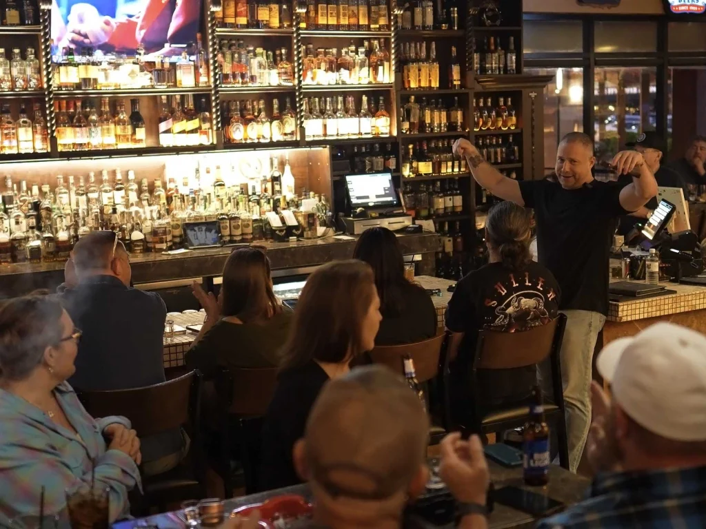 Host addressing guests seated at the bar during an event at Fox Cigar Bar Gilbert, shelves of whiskey glowing behind him