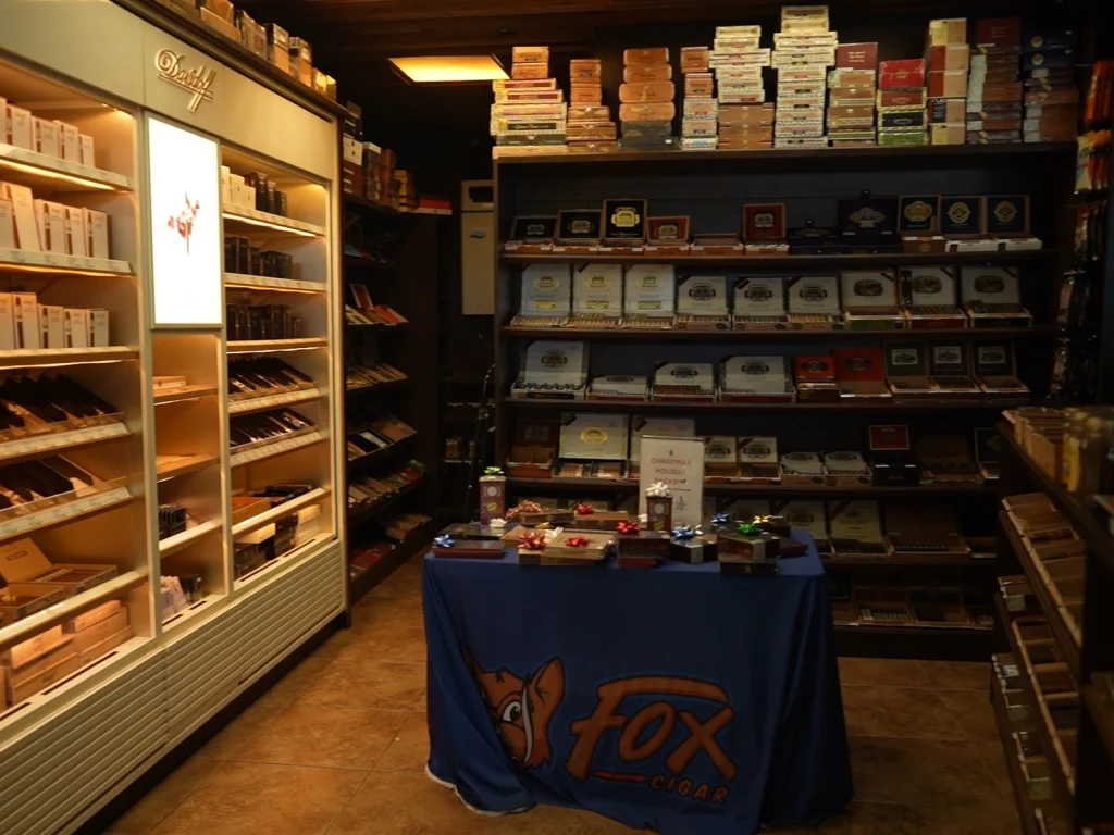 Walk-in humidor at Fox Cigar Bar Gilbert with shelves of cigar boxes and a Fox Cigar branded display table with holiday bows