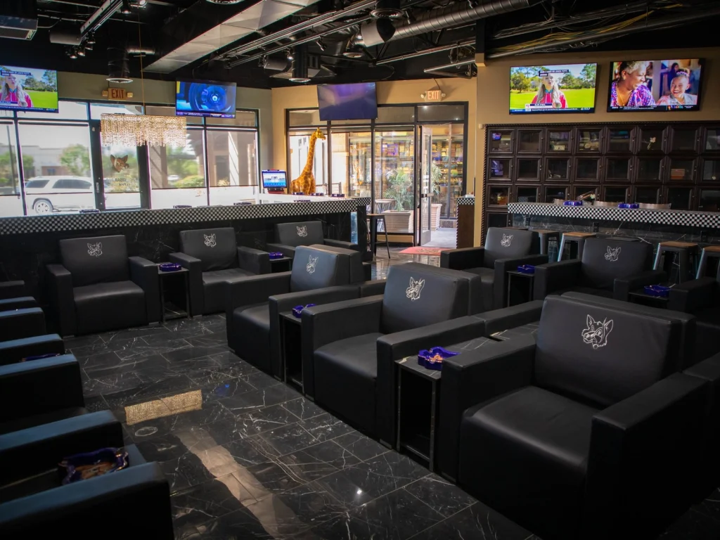 Rows of black leather fox-embossed armchairs on a marble floor in the Fox Cigar Bar Gilbert lounge, TVs and locker humidor behind