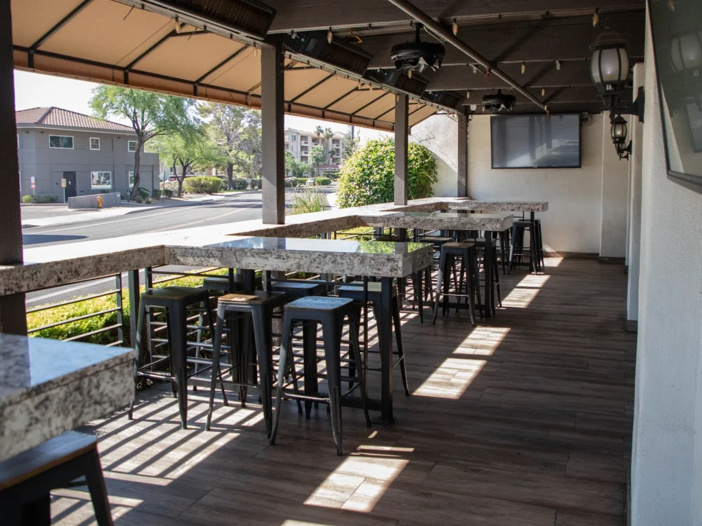 Covered patio at Fox Cigar Bar Scottsdale with granite high-top tables, metal stools, heaters and a TV in afternoon light