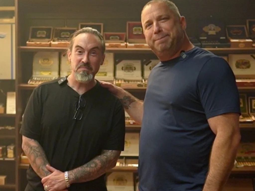 Two men posing in front of shelves of cigar boxes in the humidor at Fox Cigar Bar Scottsdale