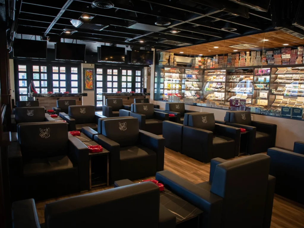 Black leather fox-logo armchairs facing the glass-walled walk-in humidor at Fox Cigar Bar Scottsdale
