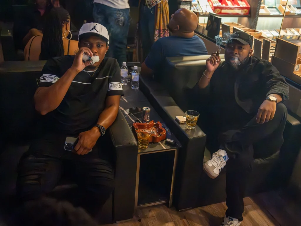 Two men smoking cigars in leather seats with whiskey and an ashtray at Fox Cigar Bar Scottsdale