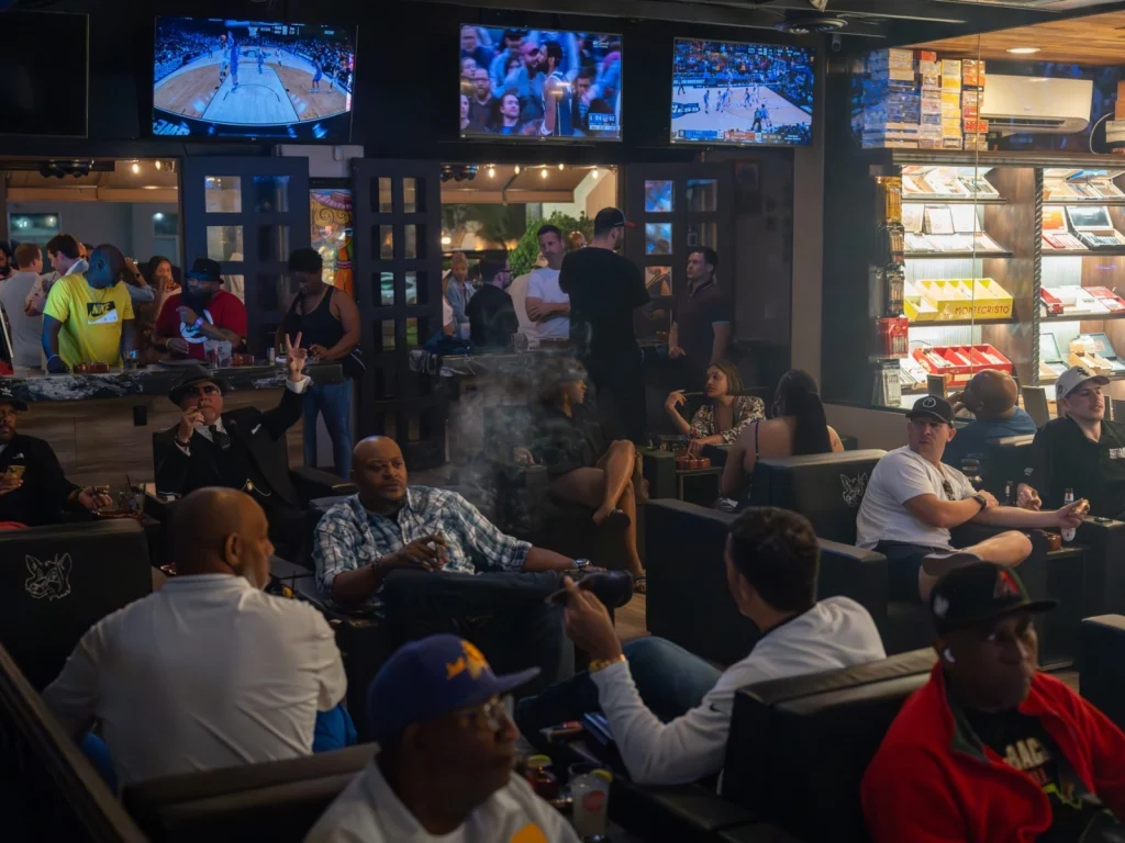 Busy game night at Fox Cigar Bar Scottsdale, guests with cigars in leather chairs under TVs showing basketball