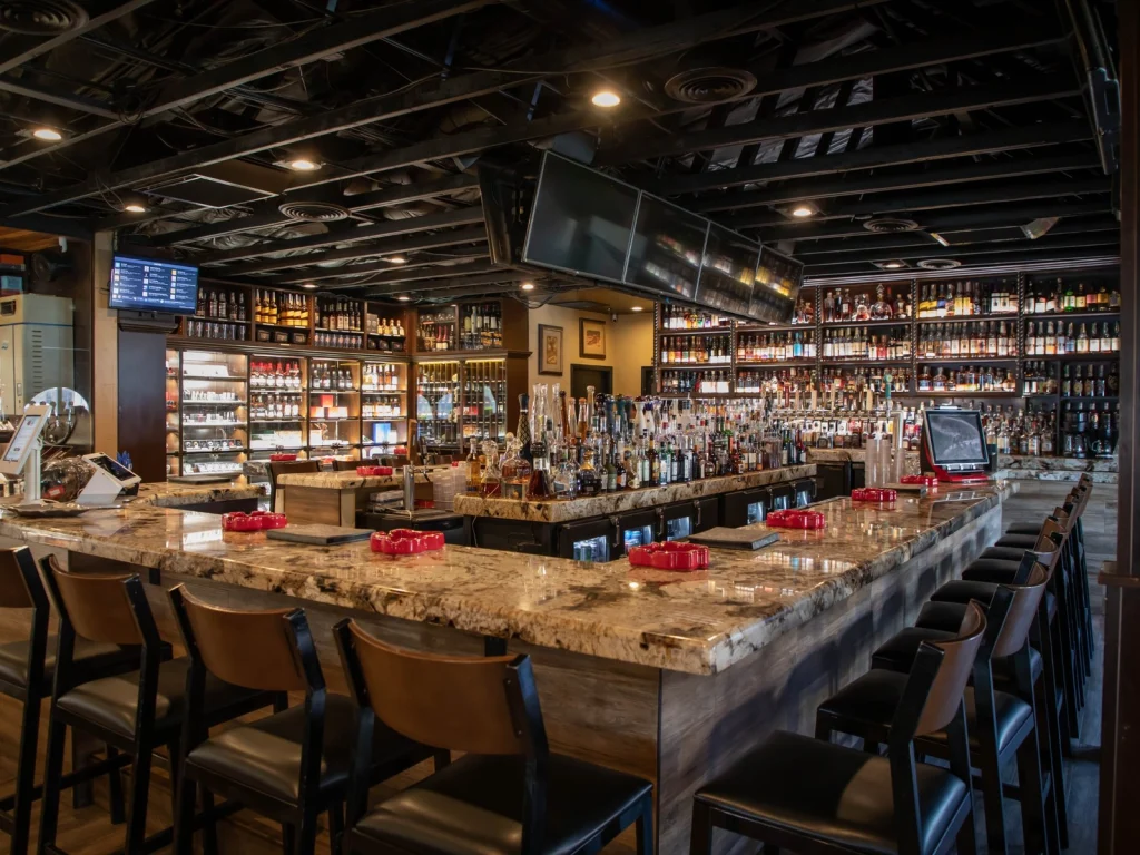 Granite-topped main bar with red ashtrays, bar stools and a wall of whiskey bottles at Fox Cigar Bar Scottsdale