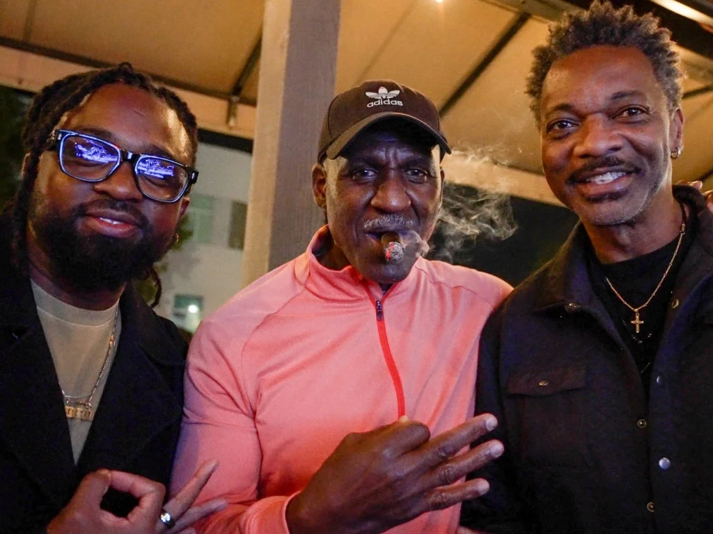 Three smiling friends pose together at night on the patio of Fox Cigar Bar Scottsdale, one with a cigar