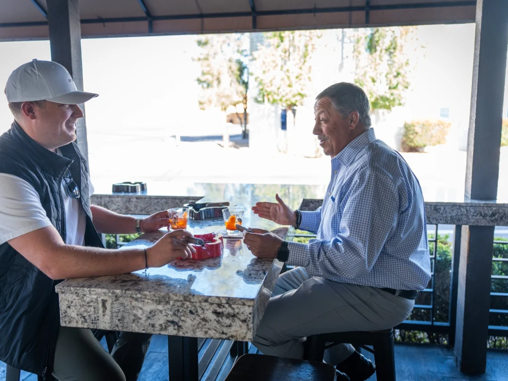 Two men chat over cigars and old fashioned cocktails at a granite patio table at Fox Cigar Bar Scottsdale
