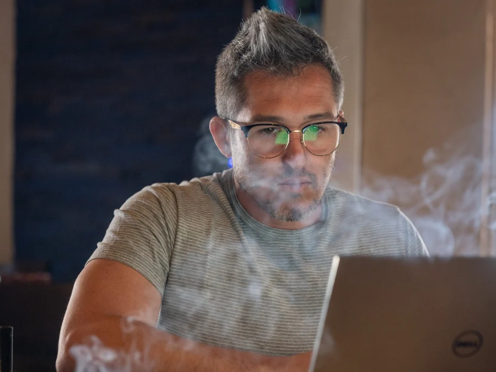 A man in glasses works on a laptop as cigar smoke drifts past in the Fox Cigar Bar Scottsdale lounge