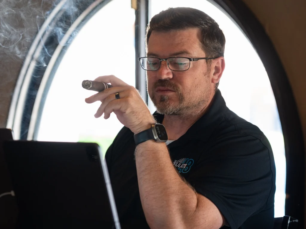 A man with glasses holds a cigar beside an arched window at Fox Cigar Bar Scottsdale, working on a tablet