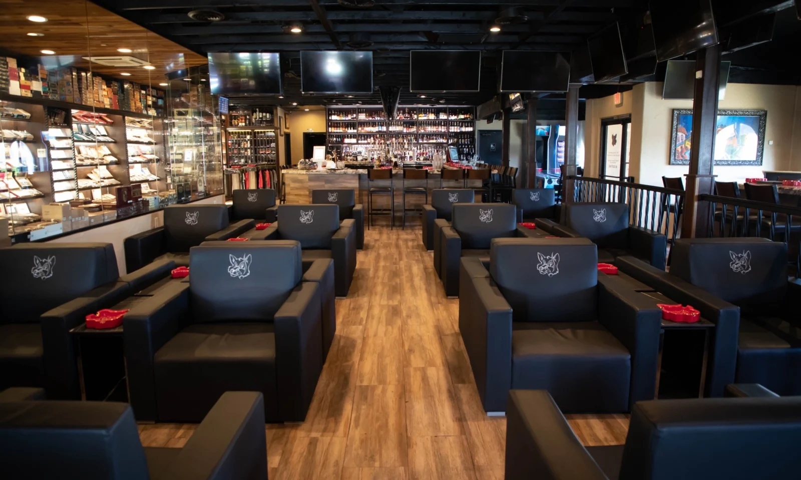 Rows of black leather lounge chairs stitched with the fox logo, the humidor on the left and the bar at the back, at Fox Cigar Bar Scottsdale