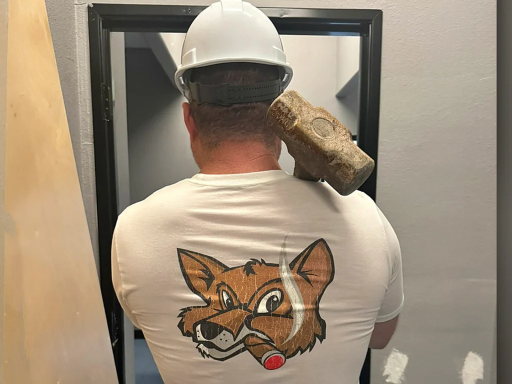 A Fox Cigar team member in a hard hat carrying a sledgehammer through a doorway on demolition day at the Surprise site