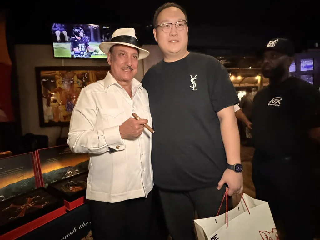 Hunter poses with Carlito Fuente beside the Arturo Fuente display, Fox Cigar bag in hand.