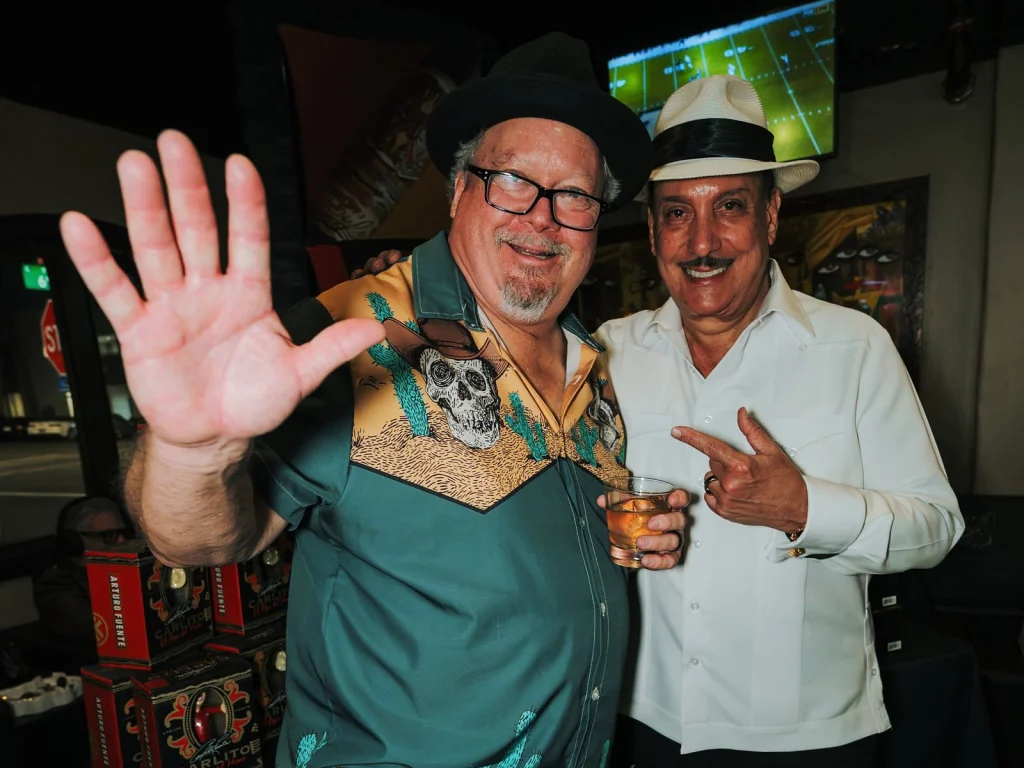 A guest throws up a high five next to Carlito Fuente in front of the Carlito “El Papo del Humo” display.