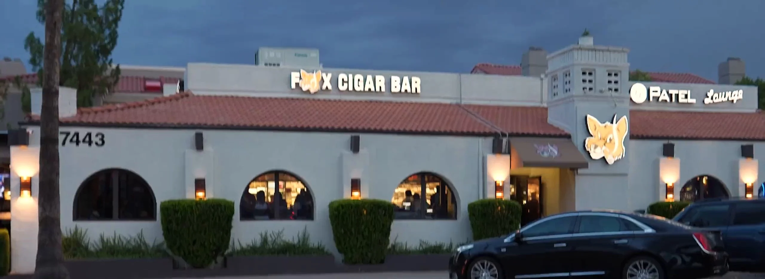Fox Cigar Bar Scottsdale at dusk: the lit FOX CIGAR BAR sign over the white stucco lounge and its arched windows